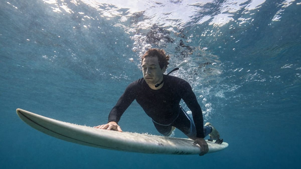 Surfer unter Wasser, ruhig und gelassen, Sonnenlicht filtert durch Wasser.
